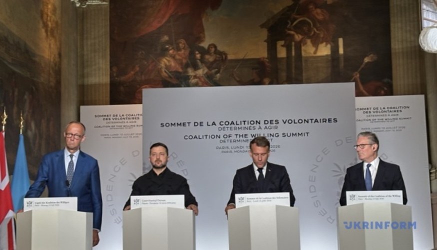 Кір Стармер, прем'єр-міністр Великої Британії, під час виступу на тлі прапорів або логотипу Коаліції охочих.
